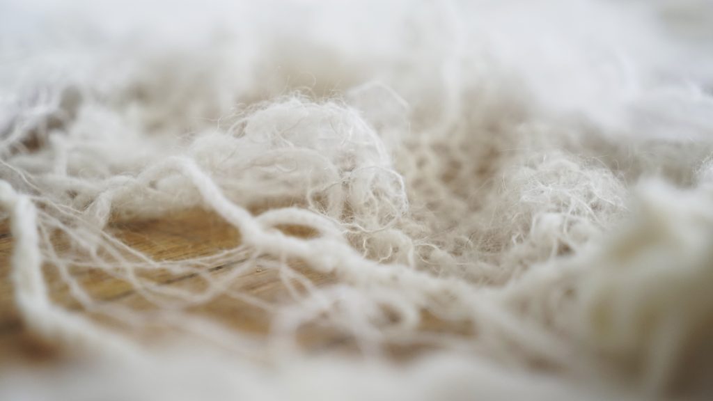 Photo featuring a close up of white wool on a wooden surface.